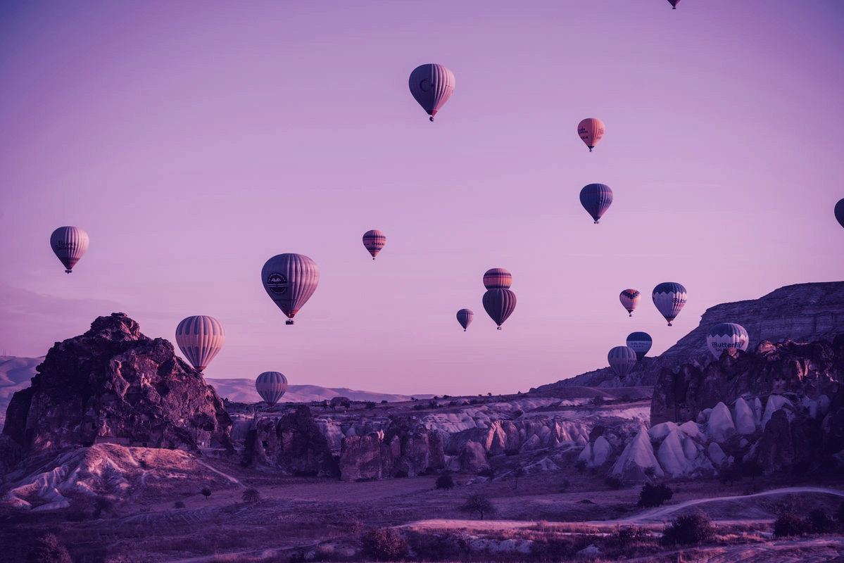 Hot air balloons floating above a sunlit rocky landscape